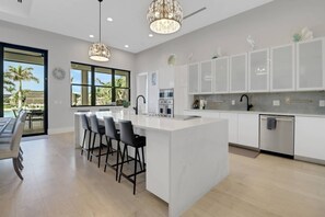 A modern kitchen with a large island, white cabinetry, and a dining area with chairs.