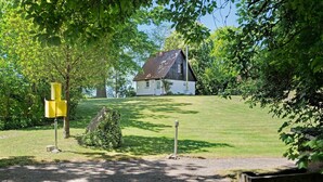 Une maison avec un toit en pente, entourée d’une pelouse et d’arbres.
