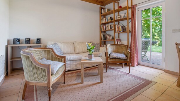 Un salon comprenant un canapé, deux fauteuils, une table basse, une bibliothèque et une porte-fenêtre coulissante donnant sur une terrasse.