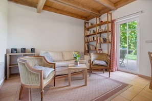 Een woonkamer met een bank, twee fauteuils, een salontafel, een boekenkast en een glazen schuifdeur naar een terras.