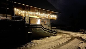 A building with a staircase leading to a door marked '10', a snow-covered path, and string lights on the roof. - Bergquelle Apartment with Mountain View, Private Terrace and Wi-Fi (Kirchzarten)
