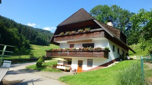 Un bâtiment à deux étages, doté d’un toit en pente, de balcons en bois ornés de jardinières et d’une allée pavée.