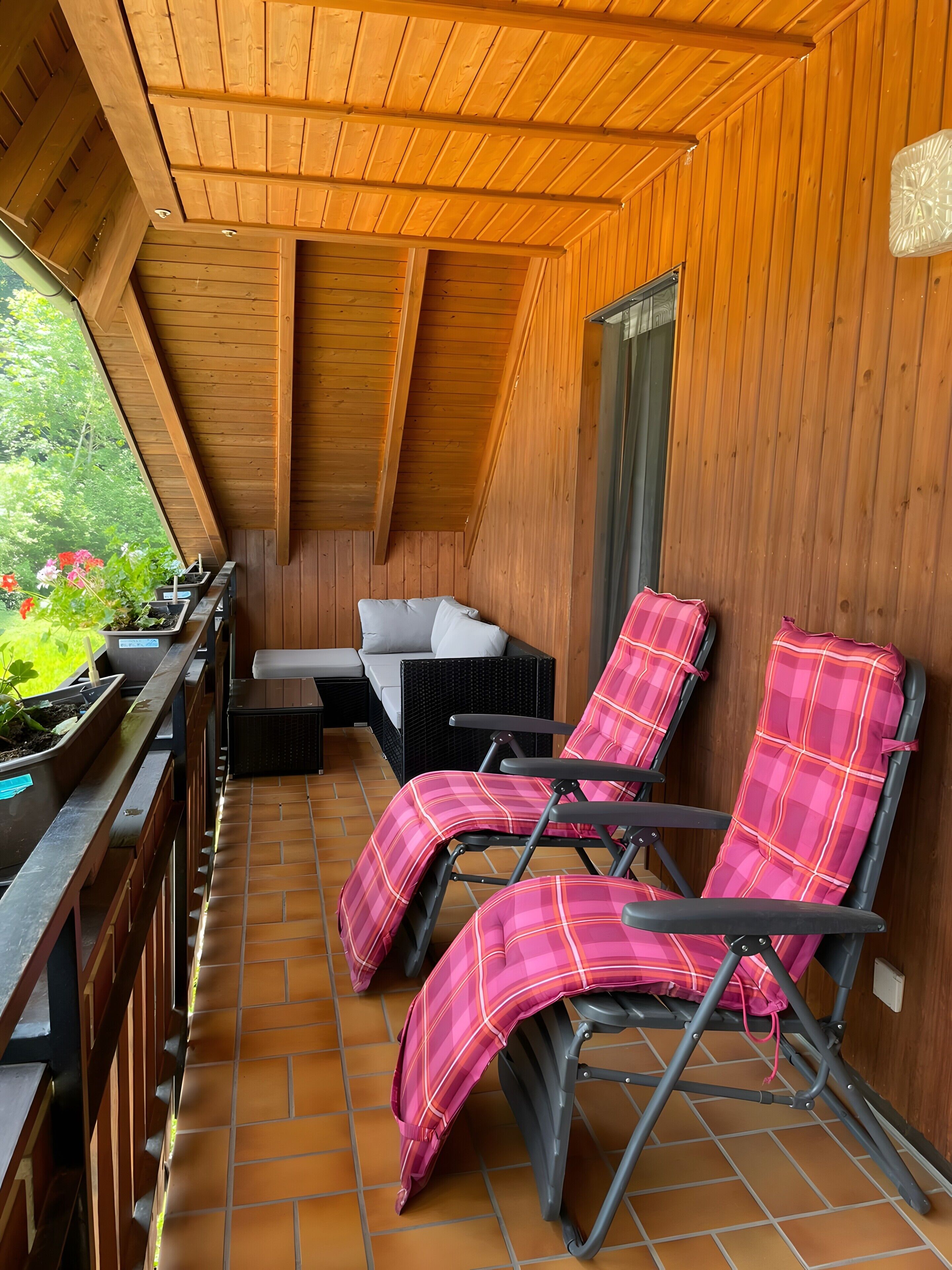 A wooden balcony with a seating area, two lounge chairs, and a small table.