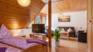 A wooden interior with a bed, TV, sofa, and a potted plant. - Apartment Lavendel with Mountain View, Shared Terrace and No Wi-Fi (Kirchzarten)