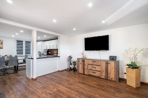 Una cocina moderna con zona de comedor, suelo de madera, televisor de pantalla plana y una orquídea en maceta.