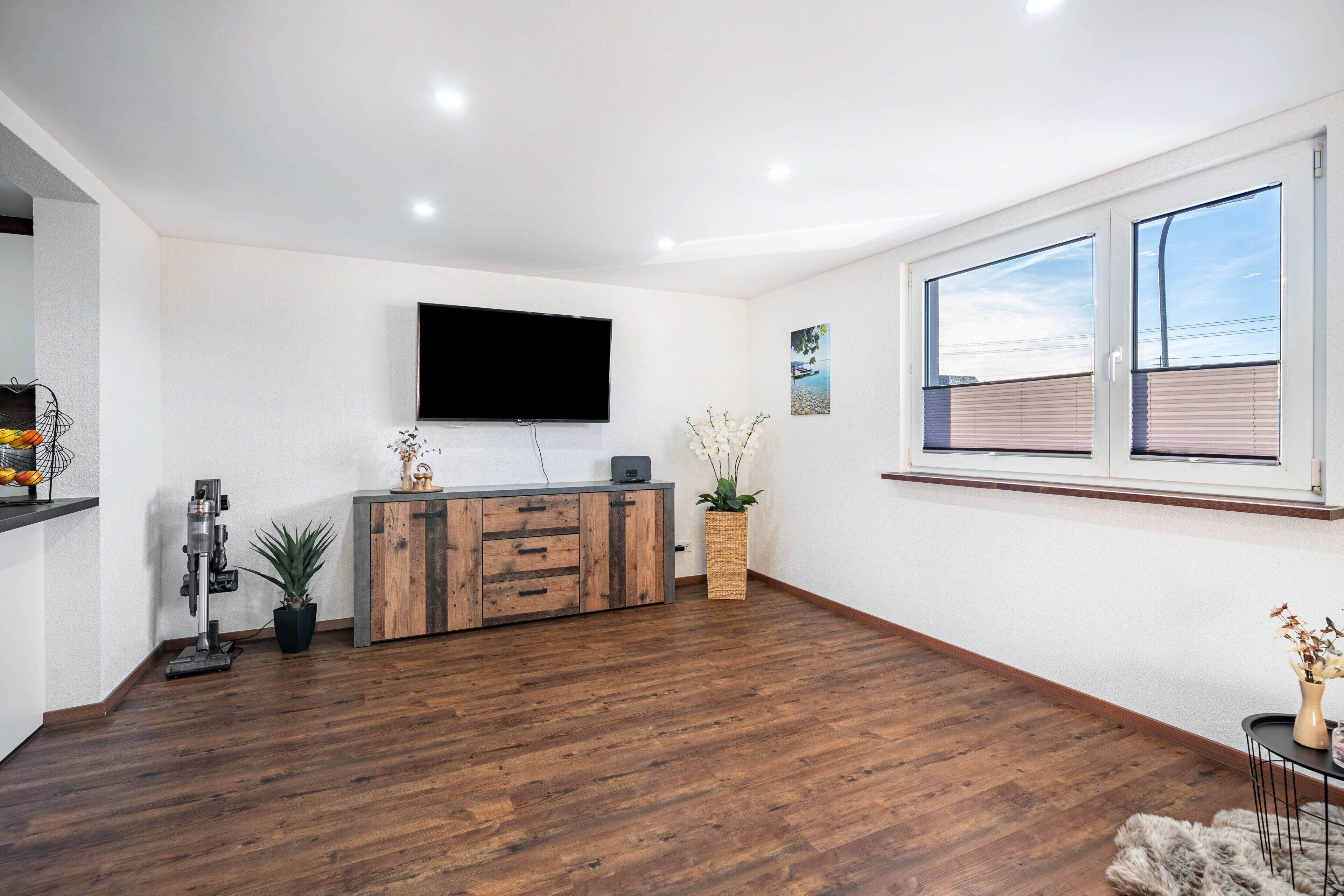 Una sala de estar moderna con piso de madera, un televisor de pantalla plana montado en la pared, un mueble de madera y un ventanal grande.