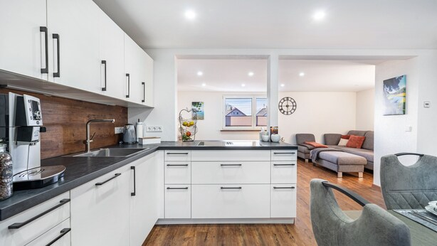 Una cocina moderna con armarios blancos, encimera negra y suelo de madera.