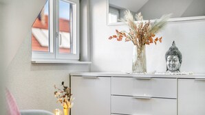 Una cocina moderna con armarios blancos, un ventanal, una estatua de Buda y un florero con flores secas.