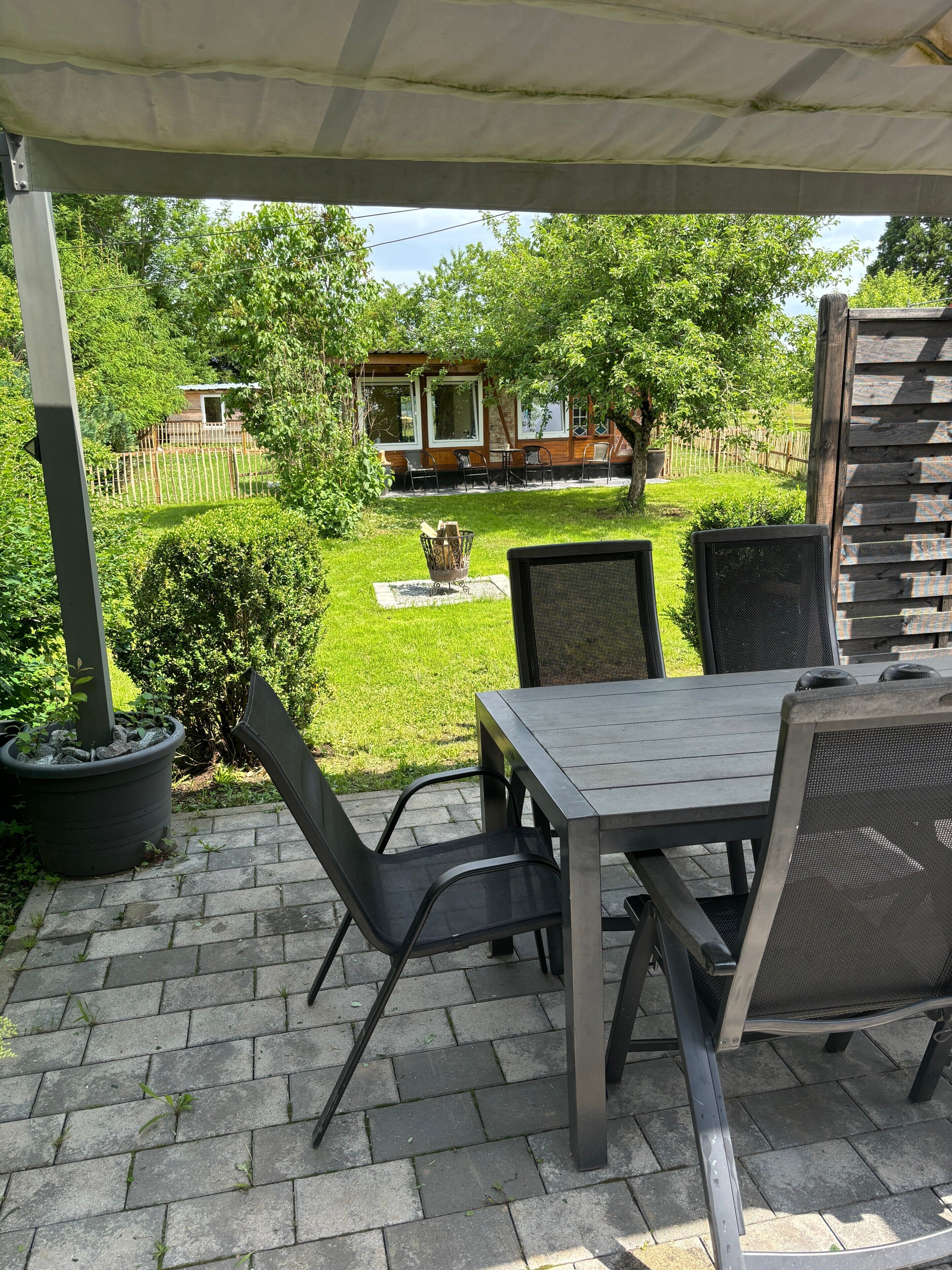 Uma área de pátio com mesa e cadeiras, um espaço de estar coberto e vista para uma casa e um jardim.