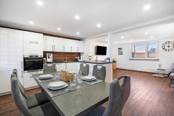 Cocina moderna con armarios blancos, una mesa de comedor lista para seis personas y un ventanal con vistas.