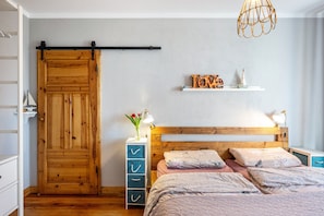 Ein Schlafzimmer mit einem Holzschrank, einem Bett mit floralem Bettzeug, einem Nachttisch mit Lampe und einem Regal mit Dekoration.