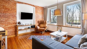 Een moderne woonkamer met een bakstenen muur, een flatscreen televisie, een lederen fauteuil, een bank, een salontafel en een groot raam met uitzicht.