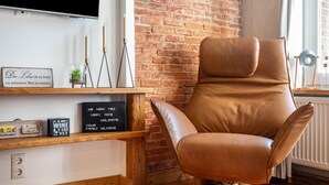 Een moderne woonkamer met een leren fauteuil, een bakstenen muur, een televisietoestel en diverse decoratieve objecten op planken.