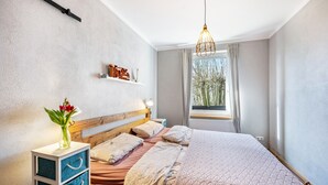 Een slaapkamer met een bed, nachtkastjes, een raam met gordijnen, een hanglamp en een plank met decoratieve objecten.