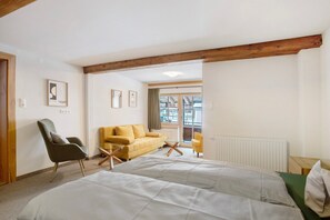 A room with a bed, a yellow sofa, a grey armchair, and a wooden ceiling beam. - Room 'Fuchswirt 09 - Doppelzimmer' with Mountain View, Shared Garden and Wi-Fi (Kelchsau)