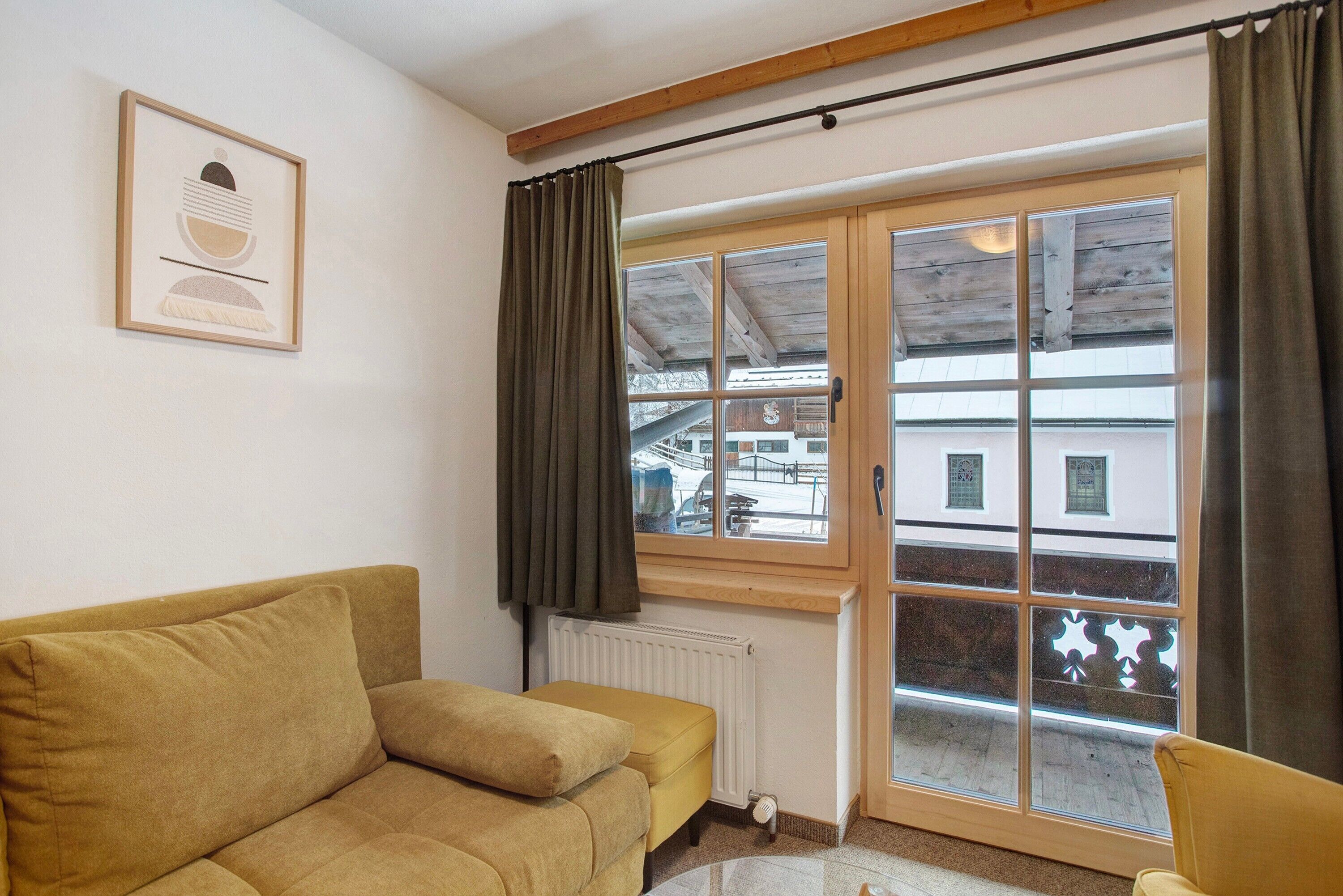 A room with a sofa, a window with curtains, a radiator, and a framed picture on the wall.