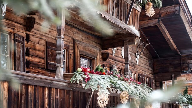 A wooden cabin with a balcony decorated with greenery and flowers.