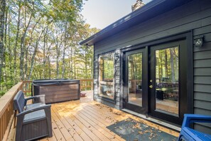 A wooden deck with a hot tub, outdoor seating, and a glass door leading to a deck area.