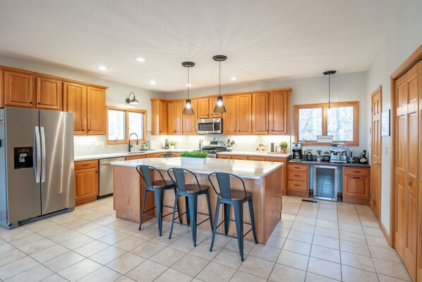 A modern kitchen with wooden cabinets, stainless steel appliances, a central island with bar stools, and pendant lighting.