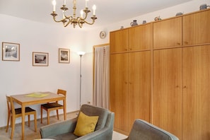 A room with a wooden dining table, chairs, a sofa, a chandelier, and a wardrobe.