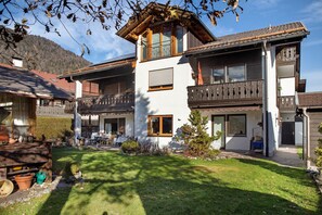 A two-story chalet with a balcony, a wooden deck, and a well-maintained garden.