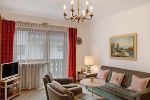 A living room with a television, sofa, chairs, a table, a lamp, and a painting on the wall.
