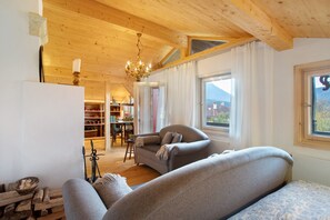 Una habitación acogedora con techo de madera, candelabro, sofá, zona de comedor y vistas a la montaña.