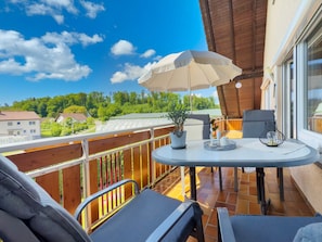 A balcony with a table, chairs, a potted plant, and a hanging chair.