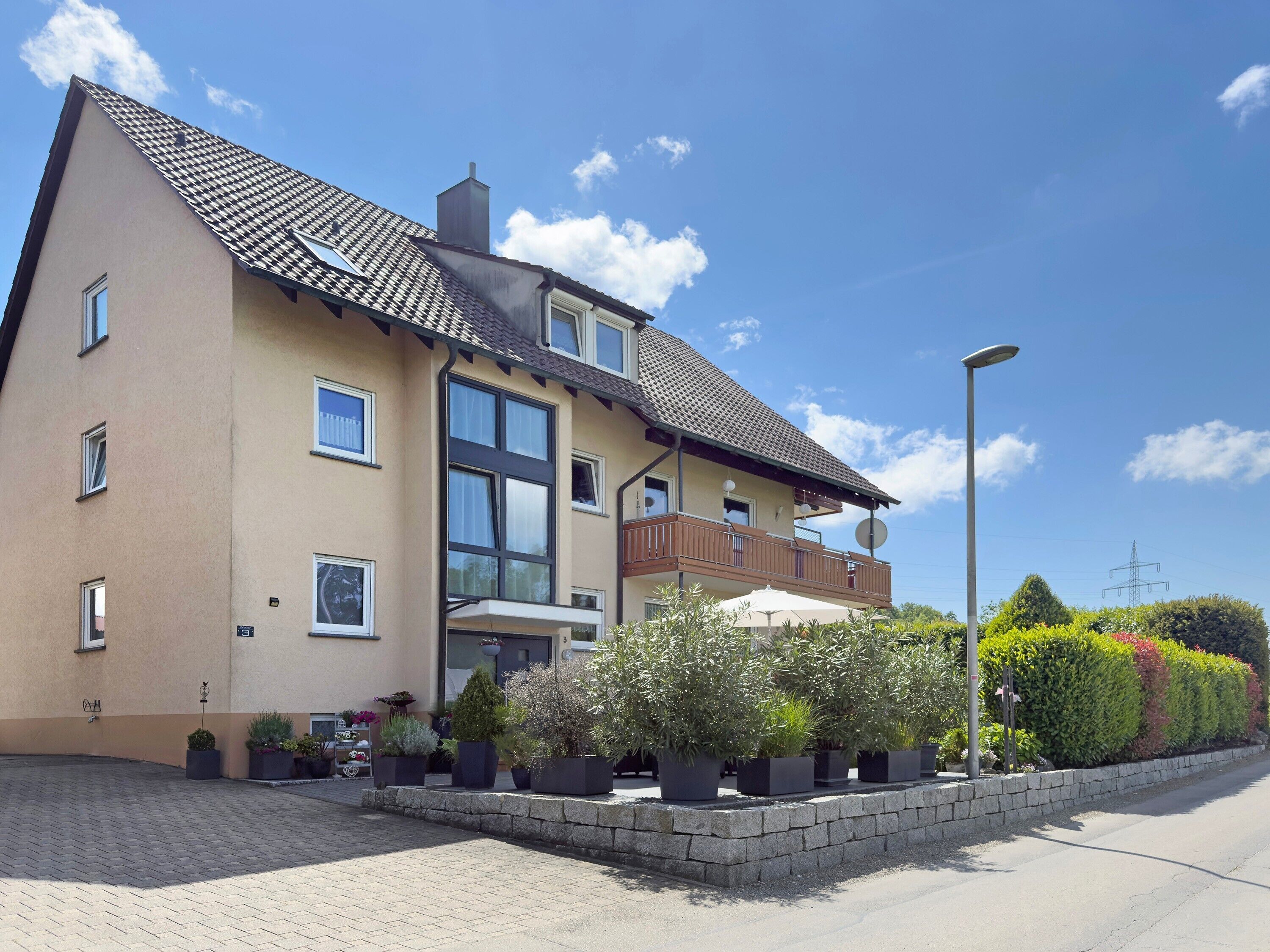 A two-story building with a tiled roof, large windows, and a balcony with outdoor seating.