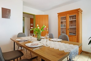 Un comedor con una mesa de madera dispuesta para cuatro personas, un florero con flores y un aparador con cristalería.
