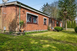 Une maison en briques avec un porche à l’avant, une plante en pot et un petit arbre.