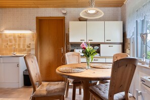 Une table à manger en bois, avec quatre chaises, un vase rempli de fleurs et, au fond, une cuisine.