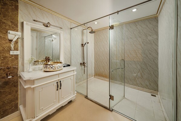 A modern bathroom with a glass-enclosed shower, marble walls, and a vanity with a gold-colored basin.