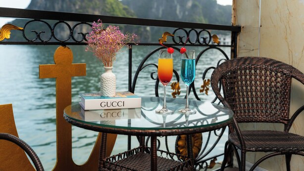 A glass table with a Gucci book, two drinks, and a vase with flowers. - Halong Aquarmarine Royal Cruise  (Tuan Chau)