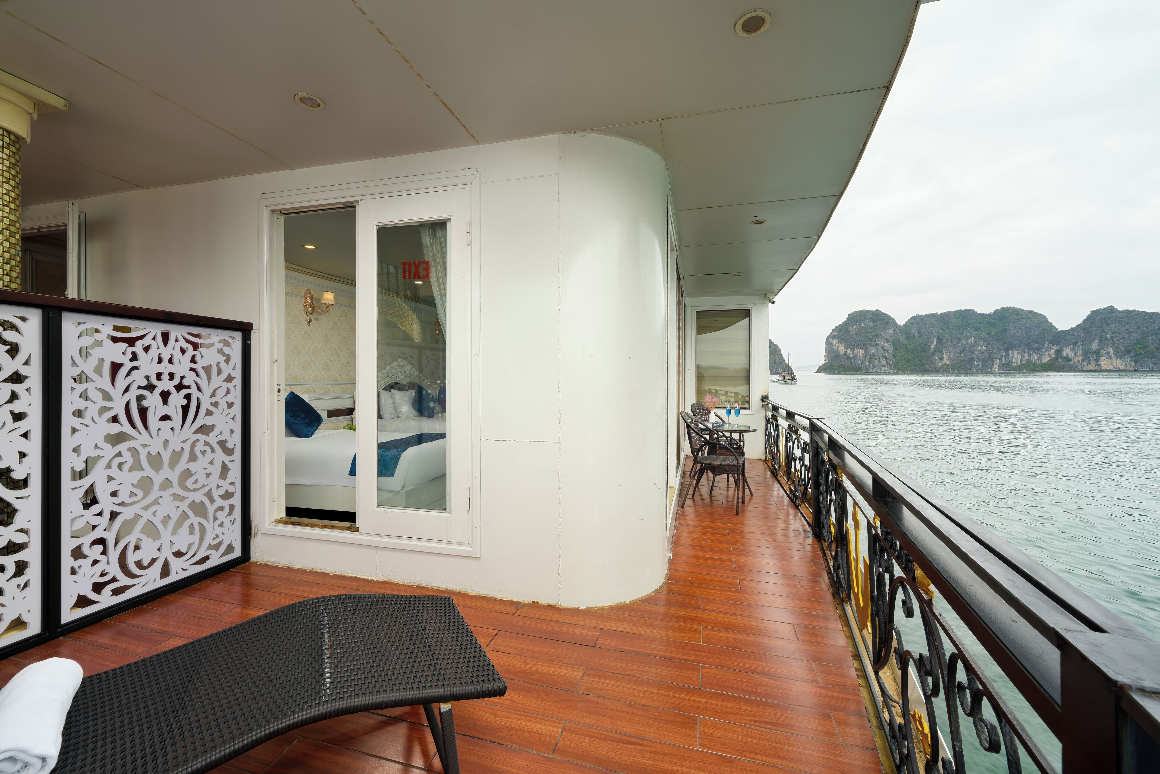 A balcony with a wooden floor, a lounge chair, a bed with a view, and a table with chairs.