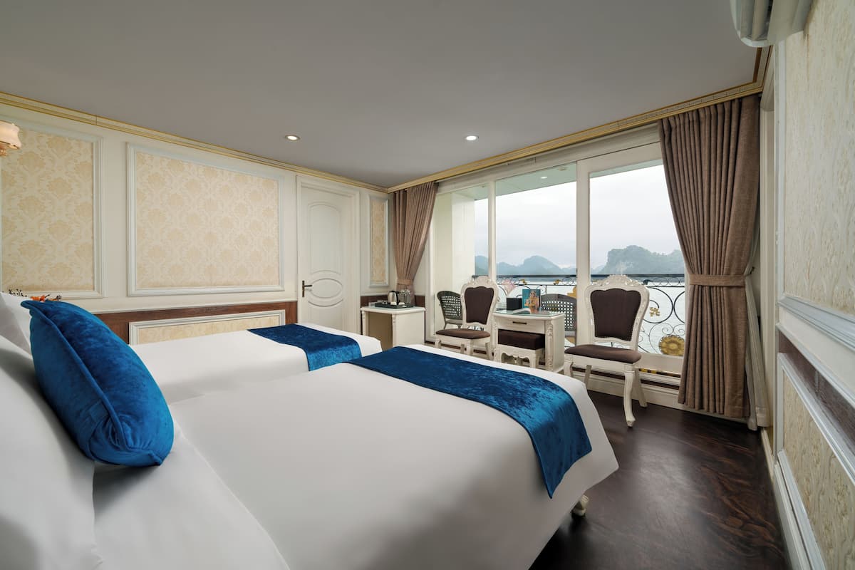 A hotel room with two beds, a desk, chairs, and a view of the sea.