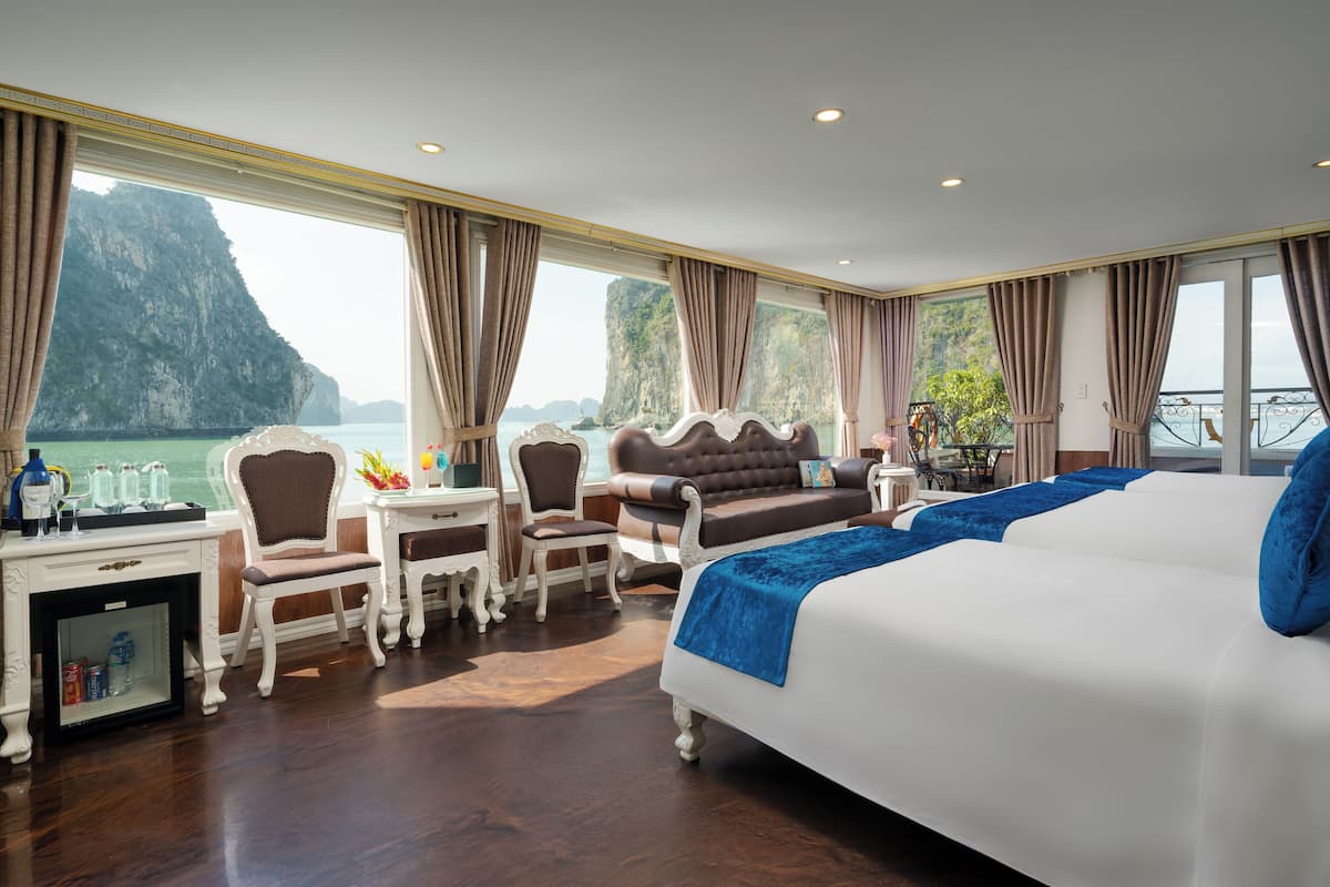 A hotel room with a large bed, a desk with a chair, a small table, and a view of a mountainous coastline.