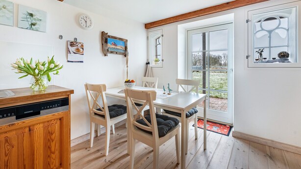A dining area with wooden chairs, a white table, and a kitchen area with a dishwasher.
