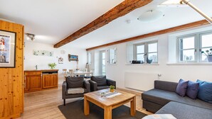A spacious living area with a wooden ceiling, a sofa, a coffee table, and a kitchen in the background.