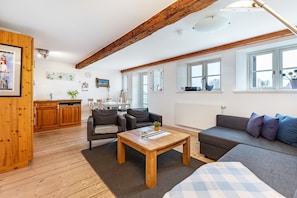 Un vaste espace de vie doté d’un plafond en bois, d’un canapé, d’une table basse et d’une cuisine à l’arrière-plan.