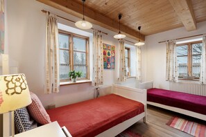 Une chambre avec deux lits, des poutres apparentes en bois au plafond, un radiateur et une fenêtre avec des rideaux.