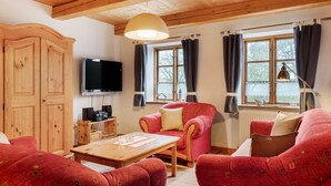 Una habitación acogedora con techo de madera, televisor, sillón rojo, mesa de madera y ventana con cortinas.
