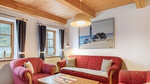 Una sala de estar acogedora con techo de madera, un sofá rojo, una mesa de centro de madera y un cuadro de un faro.