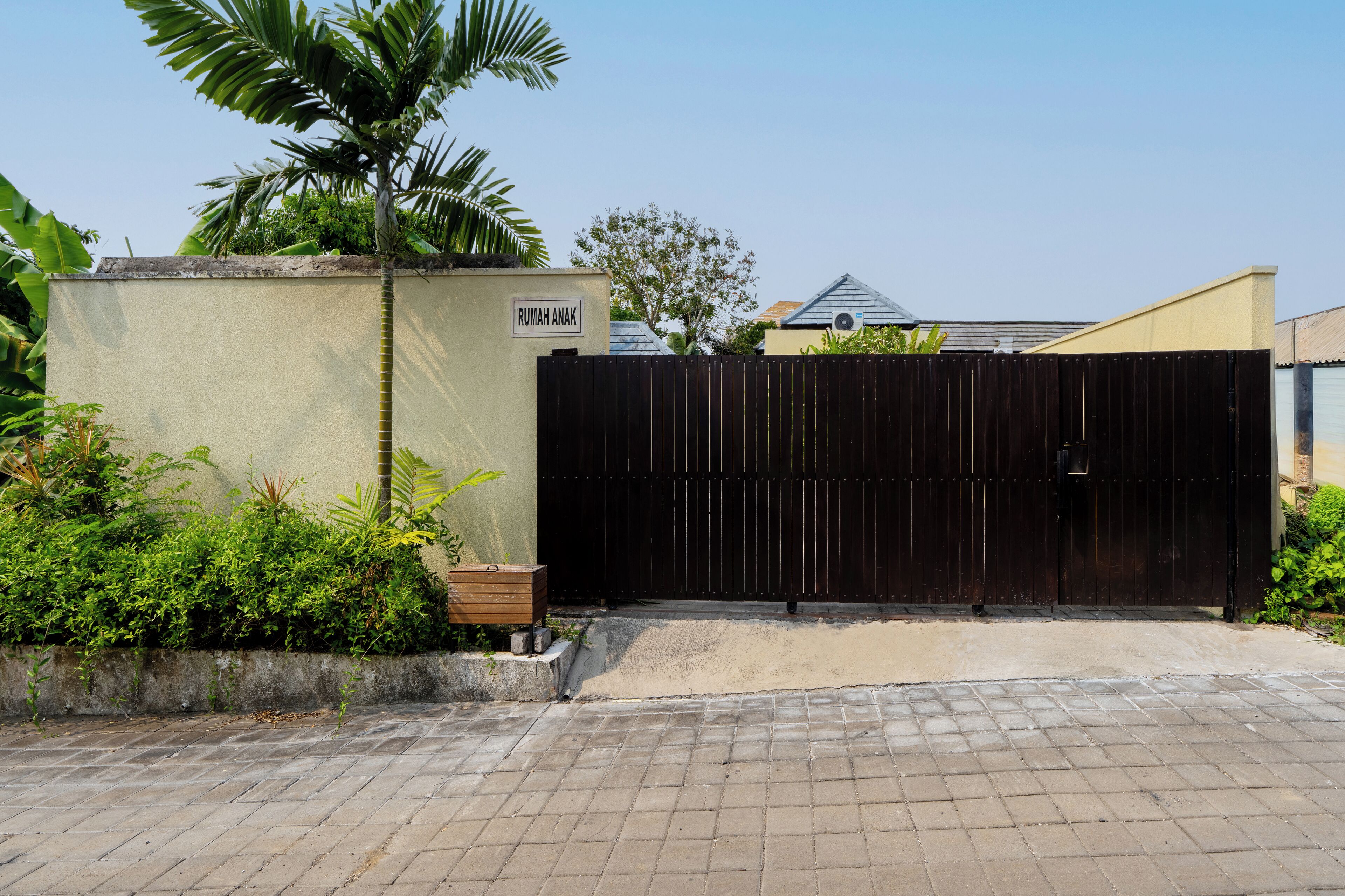 A gated entrance with a sign reading "Rumah Anak" and a palm tree nearby.
