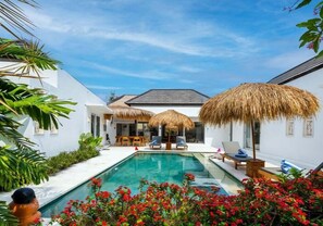 A modern poolside area with a clear pool, lounge chairs, and thatched umbrellas. - VIlla Anak by Pertama Stay (Ungasan)
