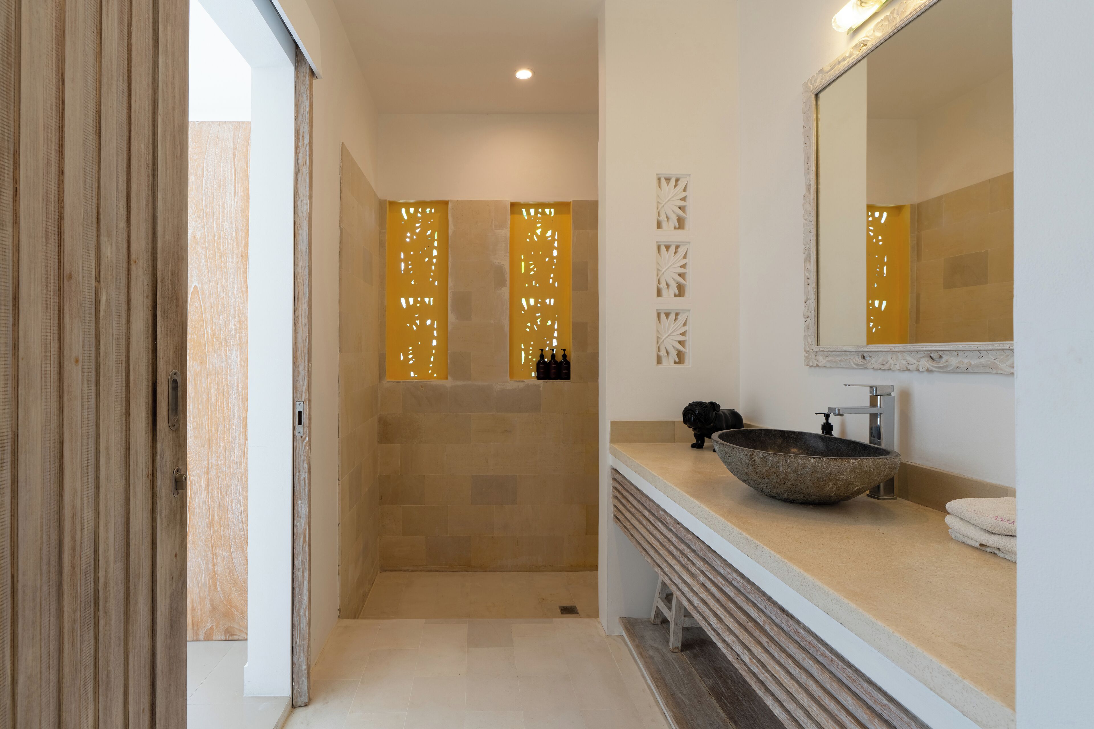 A modern bathroom with a large mirror, a stone sink, and a shower area with a wooden door.