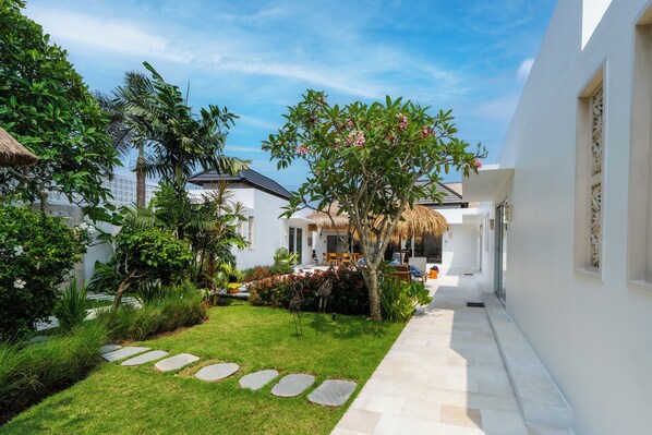 A well-maintained garden with a stone pathway, lush greenery, and a thatched-roof structure.
