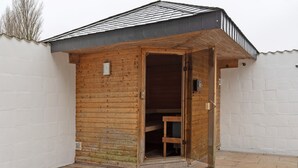 Une structure en bois avec une porte ouverte, laissant entrevoir un intérieur où se trouve un banc.
