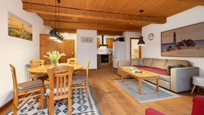 Un plafond en bois, une table à manger avec des chaises, un canapé et un coin cuisine.