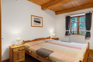 Une chambre à coucher avec un lit en bois, une table de chevet avec une lampe, une fenêtre avec des rideaux et un tableau encadré au mur.